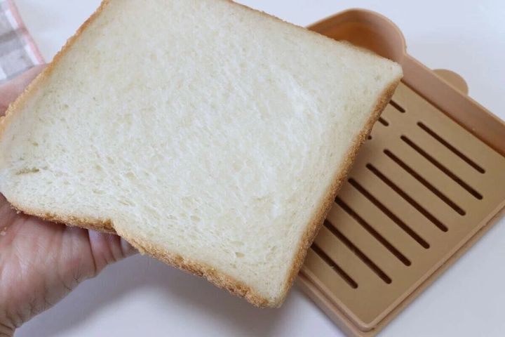手に持った食パンを食パン型調理器のすのこの上に置こうとしている