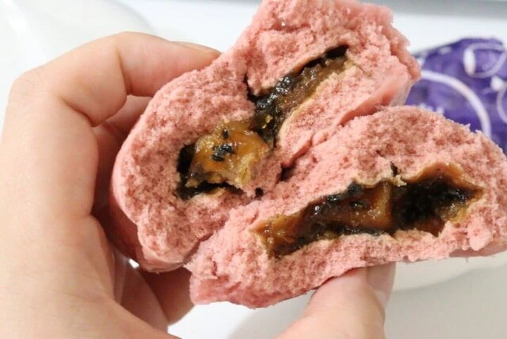 蒸されてふかふかになったピンク色の肉まんを半分に割って中身を見せている手元
