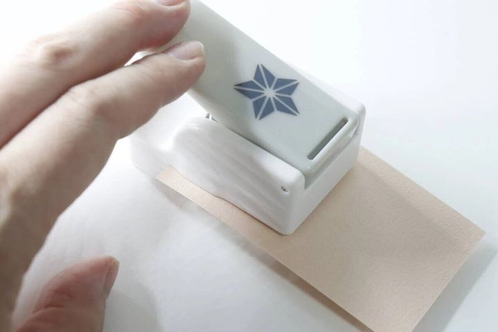 女性の指がクラフトパンチで薄い茶色の紙を挟んでパンチしている