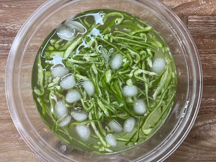 千切りピーマンが氷と水が入った透明なボウルに浸されている