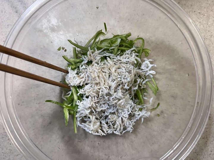 透明なボウルで千切りピーマンとしらす、調味料を箸で混ぜている