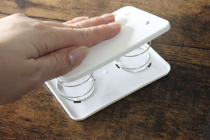 女性の手がセリアのティッシュ底上げスプリングホルダーのバネ部分を押している様子