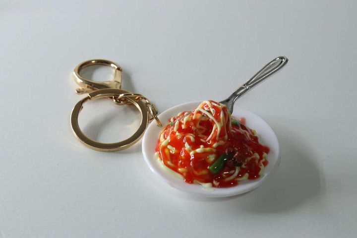 白い皿に乗ったパスタの食品サンプルキーホルダーとゴールドの金具