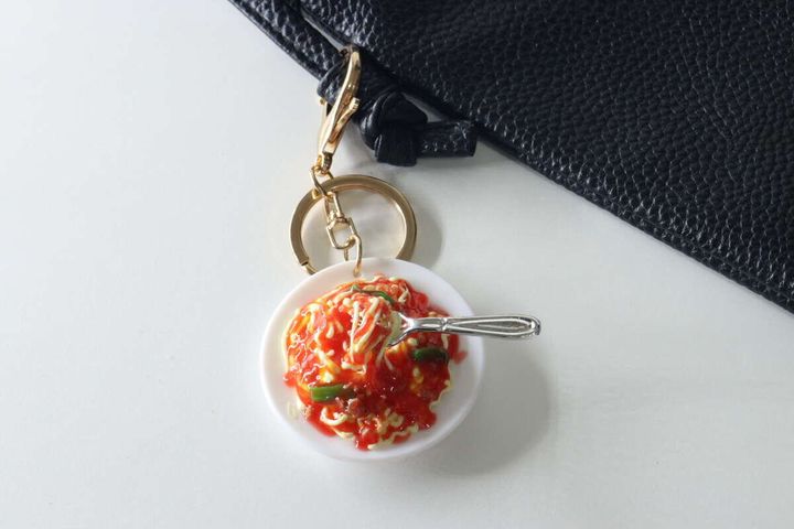 黒いバッグの持ち手に付けられたパスタの食品サンプルキーホルダー