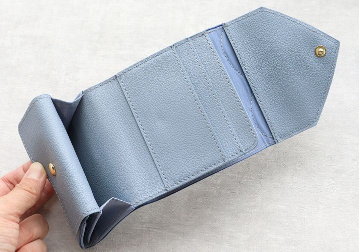 女性がサックスブルーのミニ財布を広げ、内側を見せている