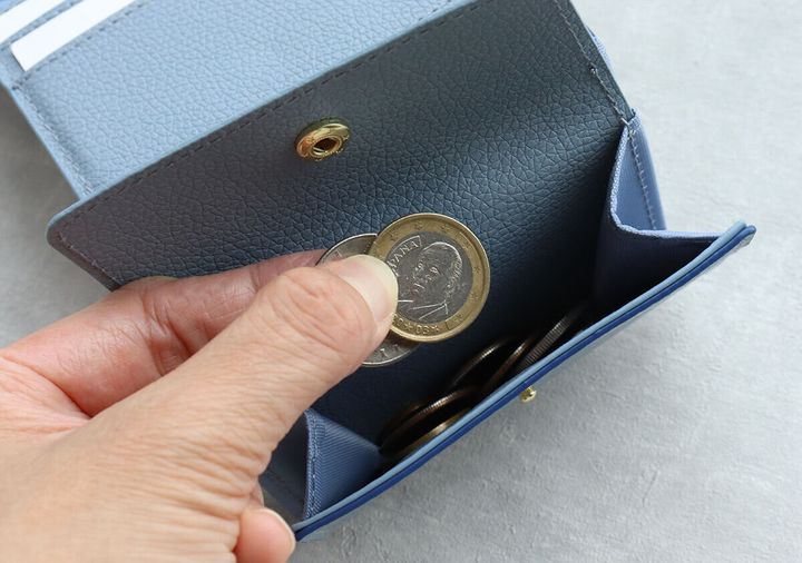 女性がサックスブルーのミニ財布の小銭入れから硬貨を取り出している