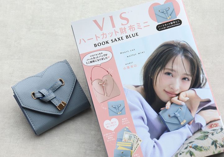 サックスブルーのハートカットミニ財布と、モデルの女性が写るブランドブック