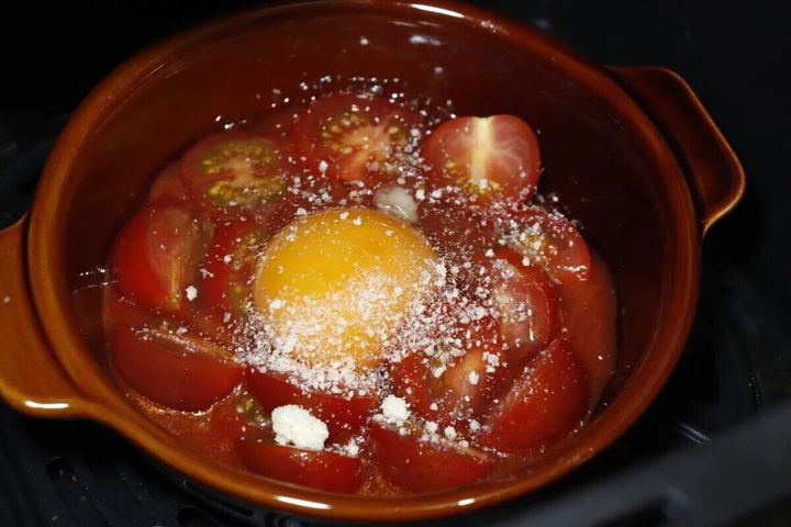 茶色のグラタン皿にミニトマトと卵、粉チーズが乗せられ、オーブンに入れる前の状態