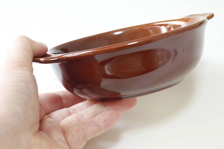手が茶色の取っ手付きグラタン皿を持っている様子