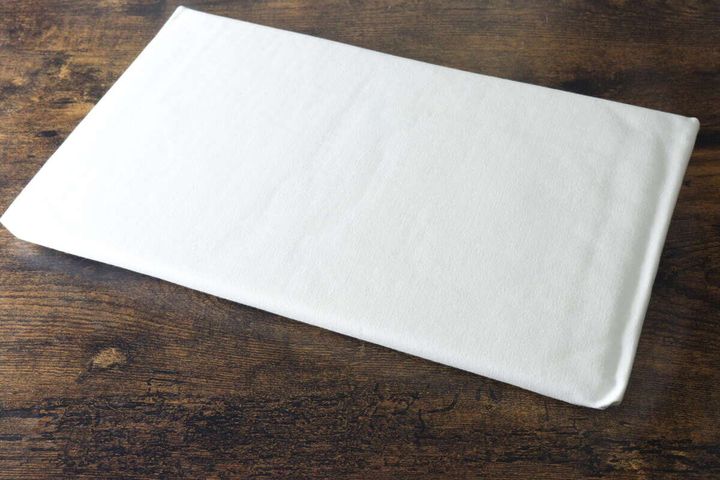 パッケージから出した白いミニアイロン台が木製テーブルに置かれている