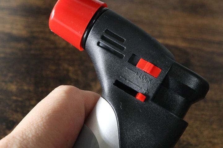手がダイソーのガスバーナーを持ち安全ロックレバーを操作している