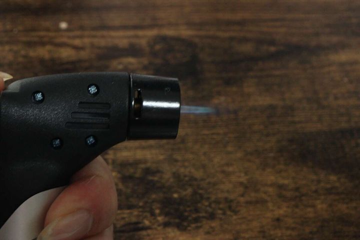 手がダイソーのガスバーナーを持ち点火ボタンを押して炎が出ている