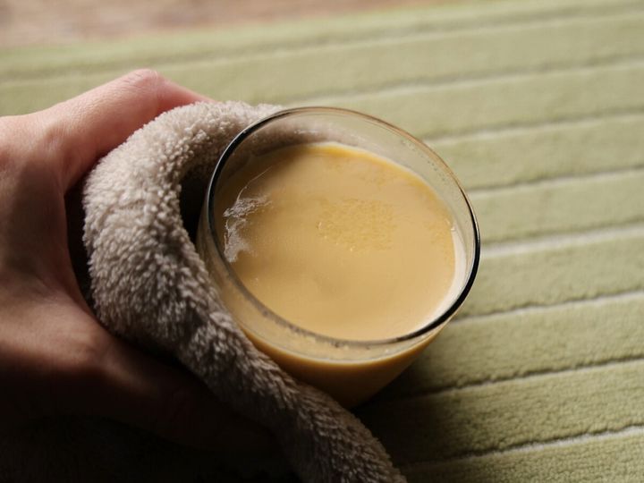 電子レンジで加熱したばかりのプリンカップをタオルで持っている手。