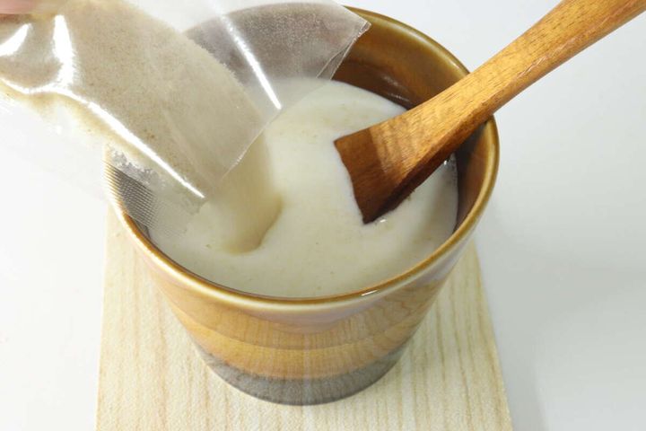 茶色のカップに入った牛乳に、ジンジャーラテの粉末を注ぎ入れる