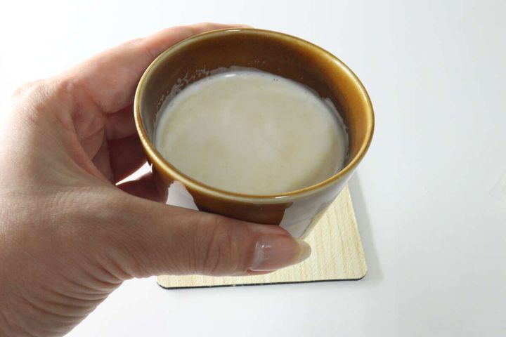 女性の手が、木製コースターに乗ったジンジャーラテのカップを持っている