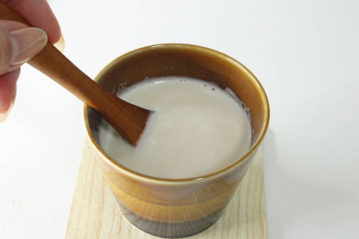 茶色のカップに入ったジンジャーラテを木製スプーンで混ぜる