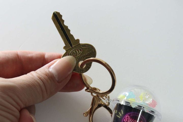 指で持たれたゴールドの鍵と、その隣にあるお菓子カップ型キーホルダーの一部