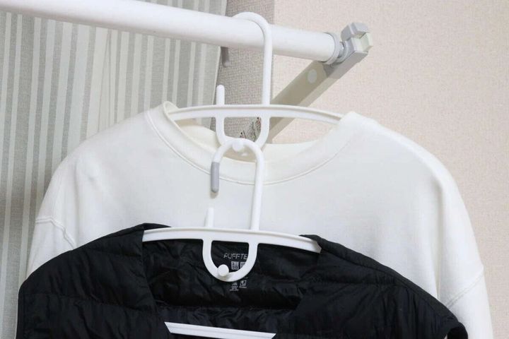 白いアーチ型連結ハンガーに白いスウェットと黒いダウンベストが掛かっている