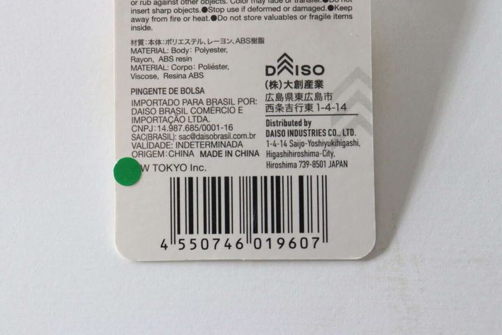 ダイソーのバッグチャームポーチの商品タグの裏面。JANコードや素材、販売元情報が記載されている。