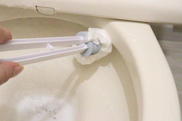 トイレットペーパーを挟んだトングで便器のフチを掃除している様子