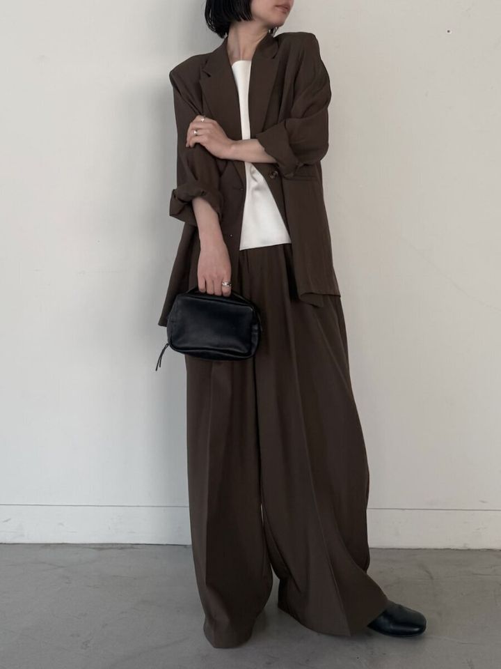 ブラウンのセットアップに白トップスを合わせ腕組みする女性