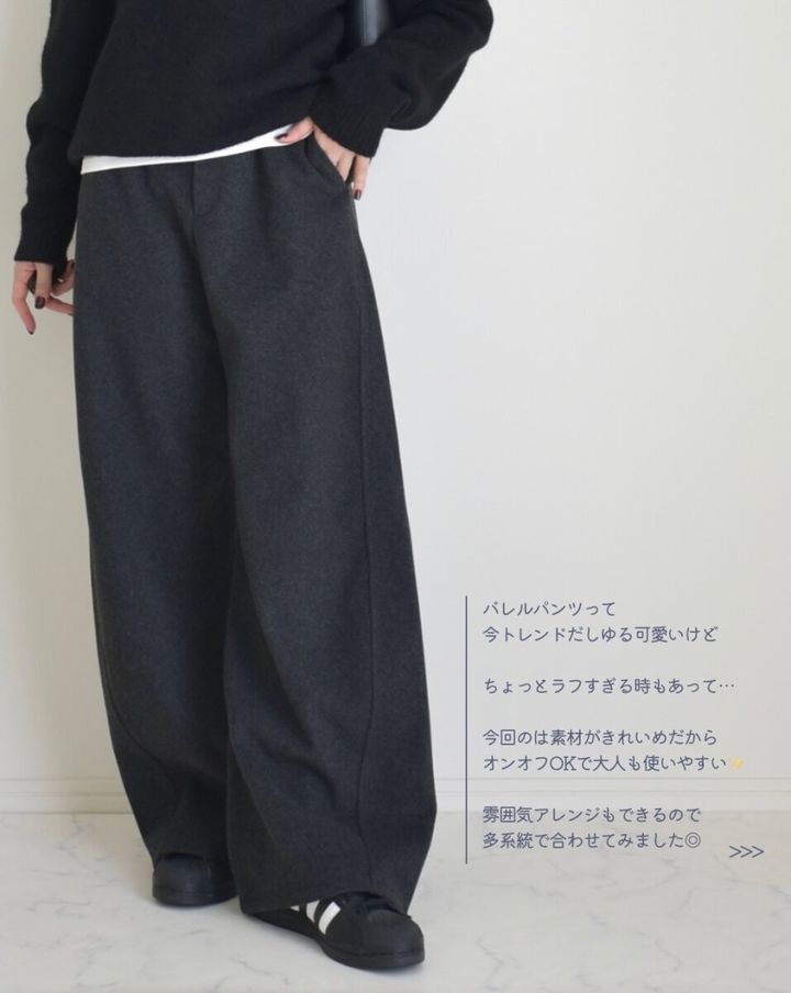 ダークグレーのバレルパンツを着用し、黒ニットと白Tシャツをレイヤードした女性の全身