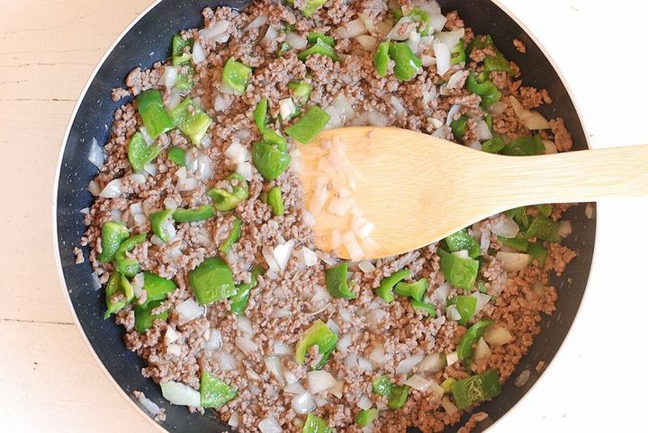 炒めたひき肉にみじん切りの玉ねぎと角切りのピーマンを加え、木べらで混ぜながら炒めている様子