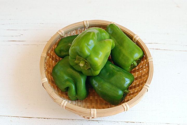 竹かごに盛られた新鮮な緑色のピーマンが5個写っている俯瞰写真