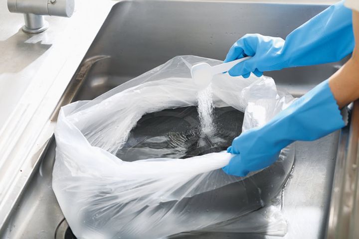 【1】二重にしたポリ袋を用意し、換気扇フィルターや五徳を入れ、40～50℃の湯をパーツがかぶるまで注ぐ。酸素系漂白剤をパッケージに記載されている量をよく溶かし、袋の口を緩く結んで15～20分つけ置きし、汚れを緩ませる。
