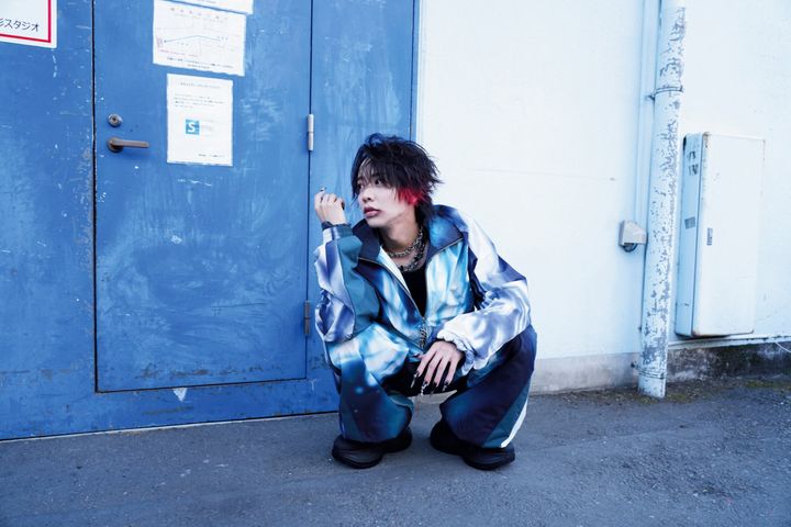 青を基調としたストリート調の衣装でしゃがみこみクールな表情を見せる松井奏さん