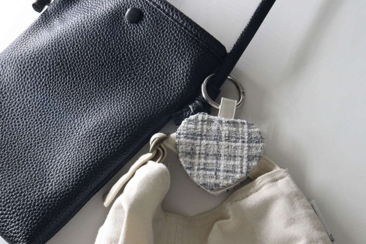 黒いショルダーバッグにツイード素材のマルチフックを取り付け、ベージュのキャップを挟んでいる