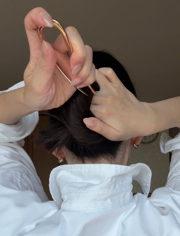 ゴールドのUピンを逆向きに持ち、髪に差し込む準備をしている様子