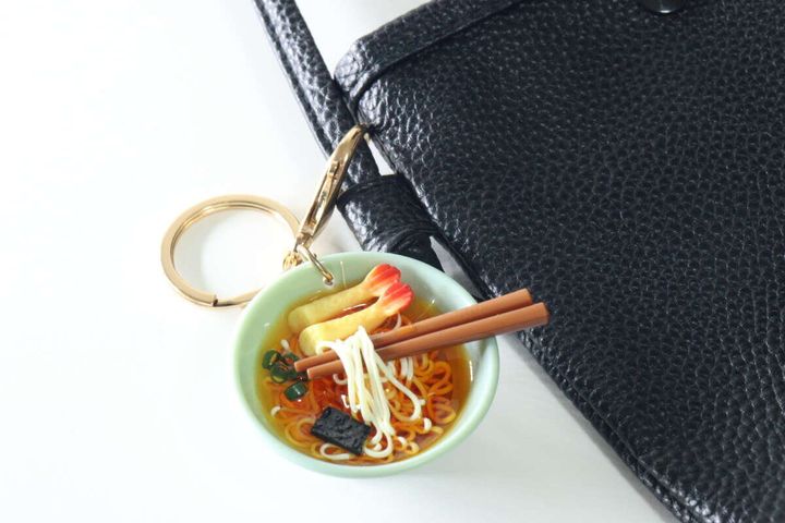 黒いバッグの持ち手に付けられたうどんキーホルダー。バッグとのサイズ感や使用イメージ。