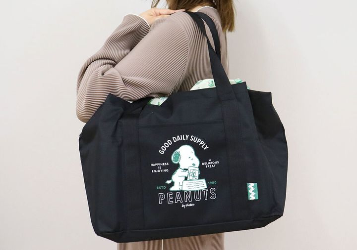 ベージュの服を着た女性が黒いスヌーピーのトートバッグを肩にかけている