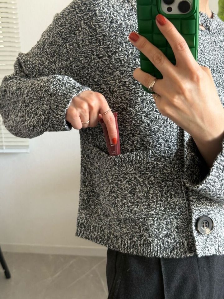 女性がツイード風カーディガンのポケットにリップを入れる