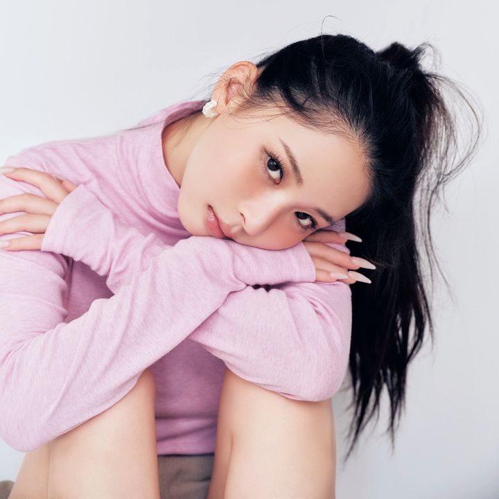 ピンクのタートルネックを着て体育座りをするモデルのミチ