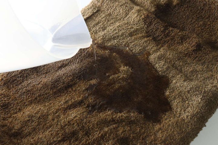 透明な容器からブラウンのバスタオルに水を注ぎ吸水性を検証している
