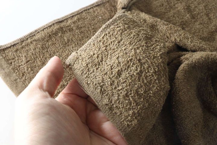 女性の手がブラウンのバスタオル生地の質感を確認している