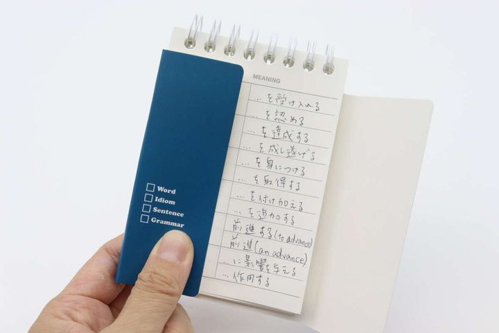 手が青い台紙で単語帳の左側（単語部分）を隠している様子