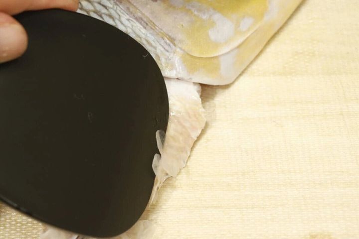 黒いしゃもじ型のうろこ取りで魚の胴体のうろこを剥がしている様子