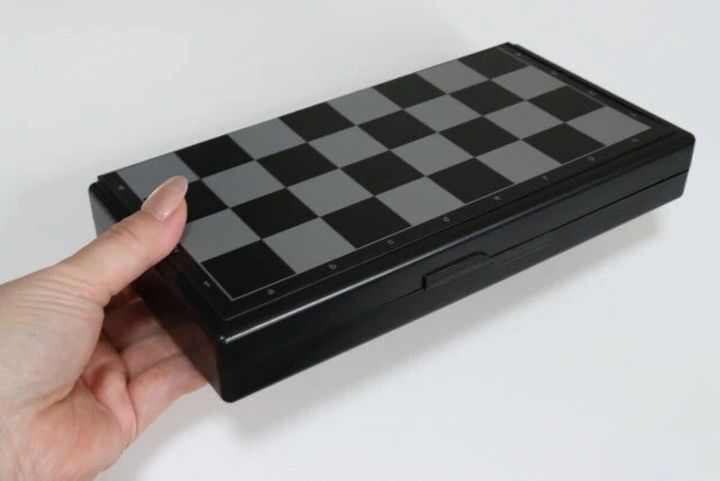 黒とグレーのチェック柄の折りたたみ式チェス盤を片手で持っている様子
