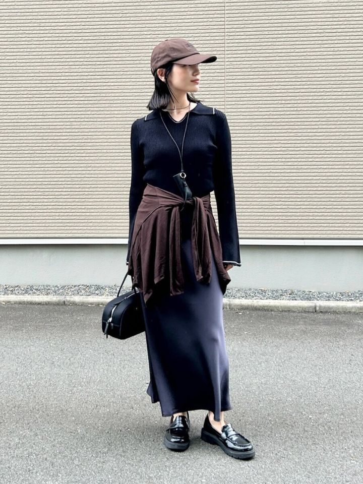 黒のリブニットとグレーのナロースカートを着用し、ブラウンのシャツを腰巻きした女性