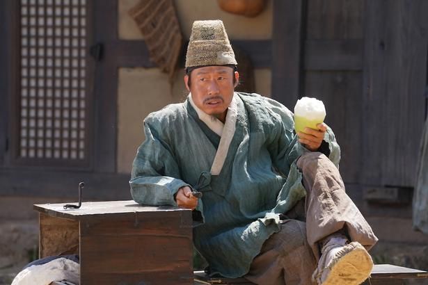 奔走する村人を横目に果物を頬張るフンド [c] 2026 SHOWBOX, ONDA WORKS AND B.A. ENTERTAINMENT ALL RIGHTS RESERVED.