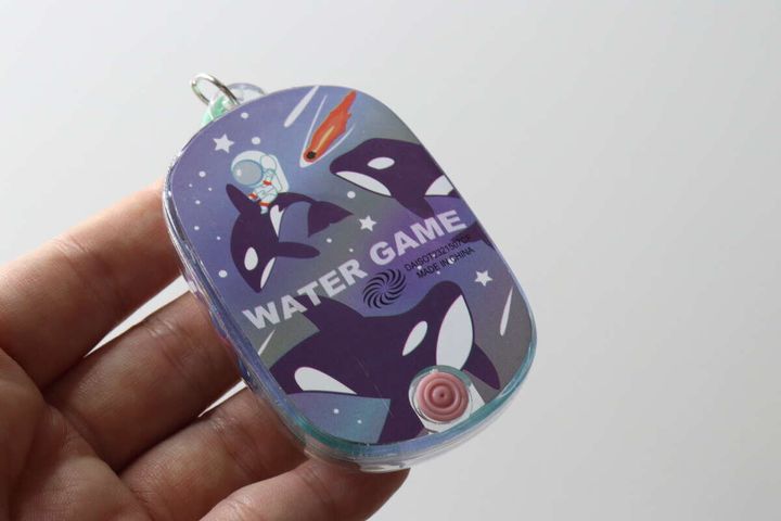 手のひらに乗せたミニウォーターゲーム機の裏側。宇宙服のシャチが描かれている