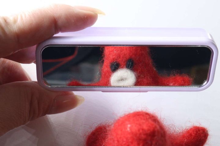 女性の指が持っている「ちょこっとケース ミラー付き」の鏡に、赤いタコのぬいぐるみが映り込んでいる