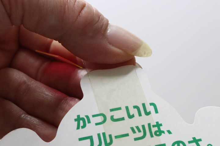 「かっこいいフルーツは」と書かれたポスターの裏にテープを貼る指先