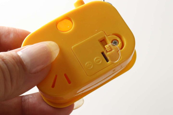 カメラ型キーホルダーの裏側。電池カバーが開いており、絶縁シートが差し込まれている。