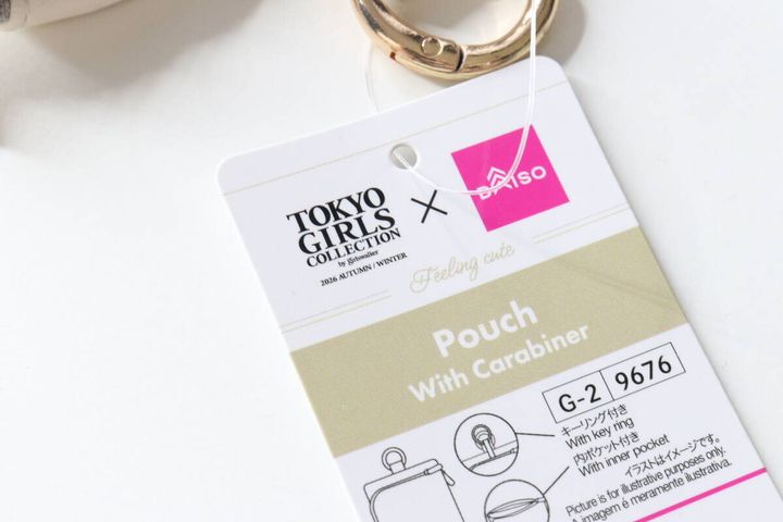 白い背景に置かれた、ポーチのタグの表面。TGCコラボのロゴと商品名が写っている