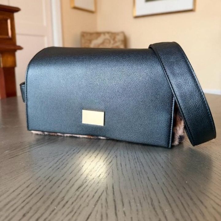 黒いレザー調のショルダーバッグ。下部にレオパード柄が見え、ゴールドのプレートがアクセントになっている。