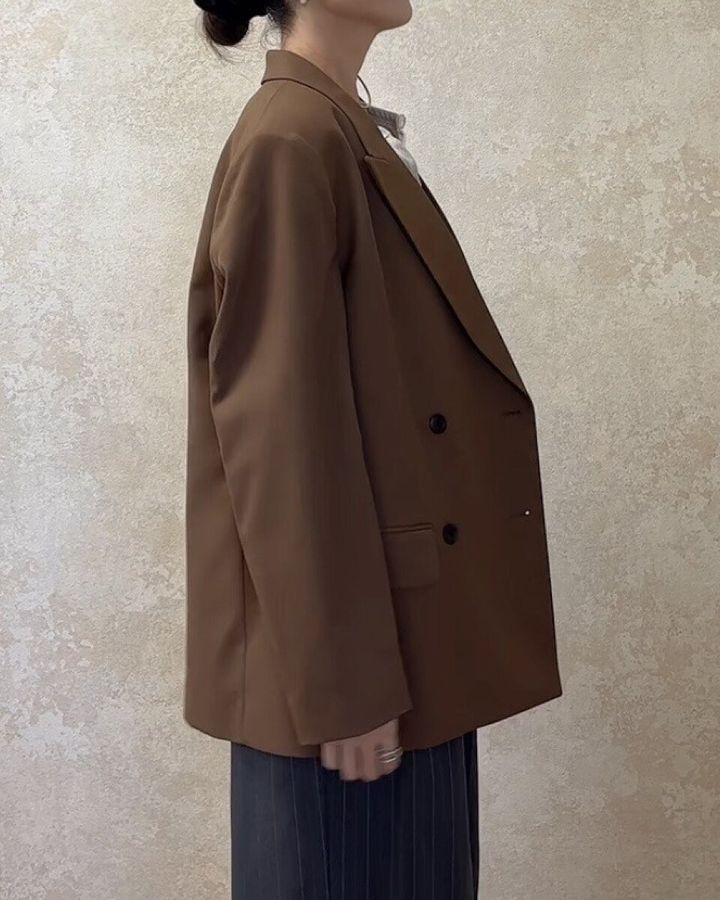 ブラウンのジャケットとストライプパンツを着用した女性の横向き全身